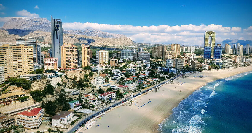 Langer Sandstrand und dahinter viele Gebäude und Hotels.