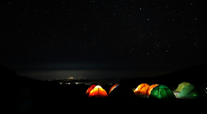 Beleuchtete Zelte in der dunklen Nacht mit vielen kleinen Sternen am Himmel.