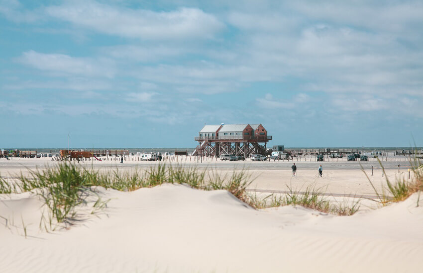 Ein breiter Sandstrand mit einem Pfahlbau mitten drin.