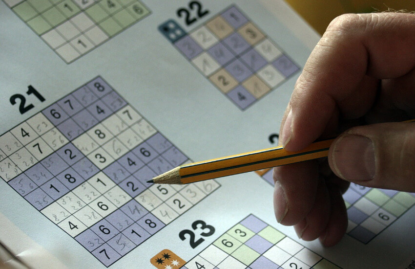 Ein Sudoku Heft, wo eine Hand mit einem Bleistift abgelegt ist.