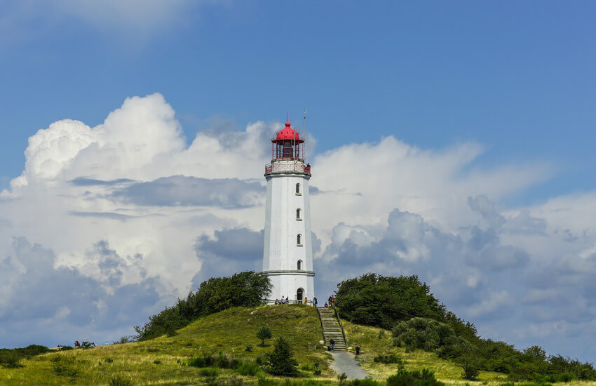 Ein weißer Leuchtturm auf einem Hügel, umgeben von Sträuchern und Wiesen.