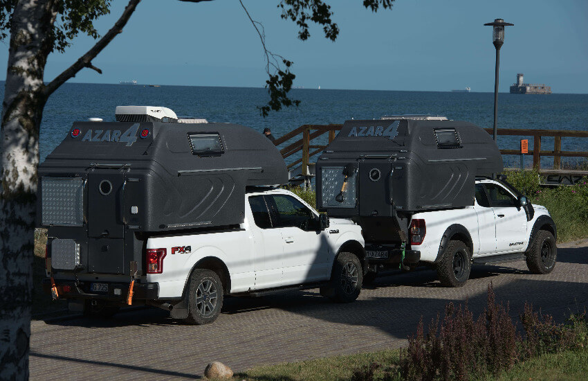Zwei weiße Pickup mit einem dunkelgrauen Camperaufbau parken nahe vom Meer.