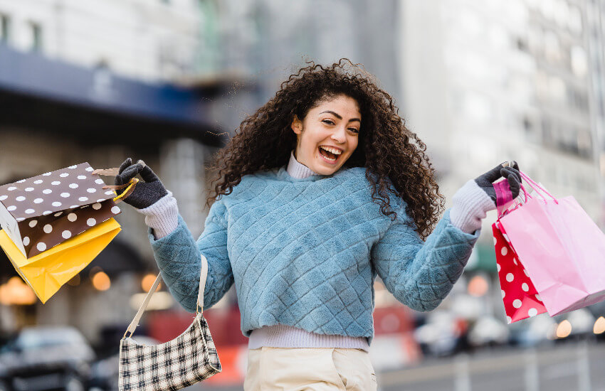 Eine Frau mit bunten Einkaufstaschen freut sich über die erworbenen Schnäppchen.