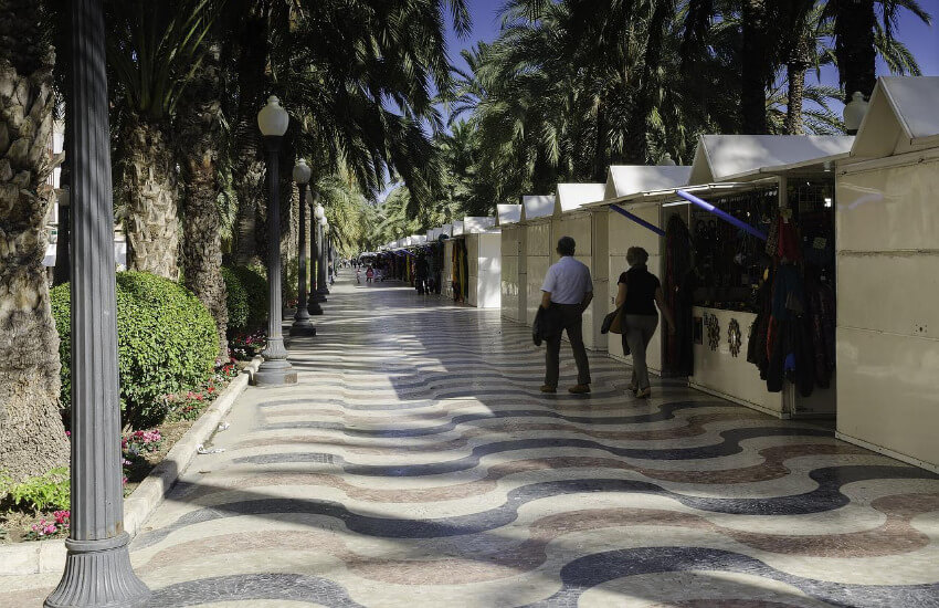 Eine Promenade mit welligen buntem Pflaster und Palmen auf beiden Seiten.