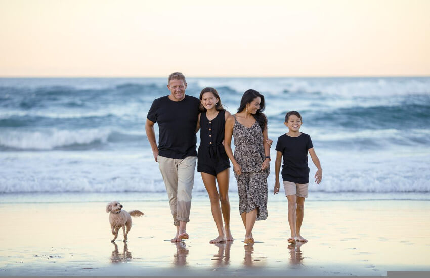 Eine Familie mit 2 Kindern und einem Hund gehen am Strand spazieren.