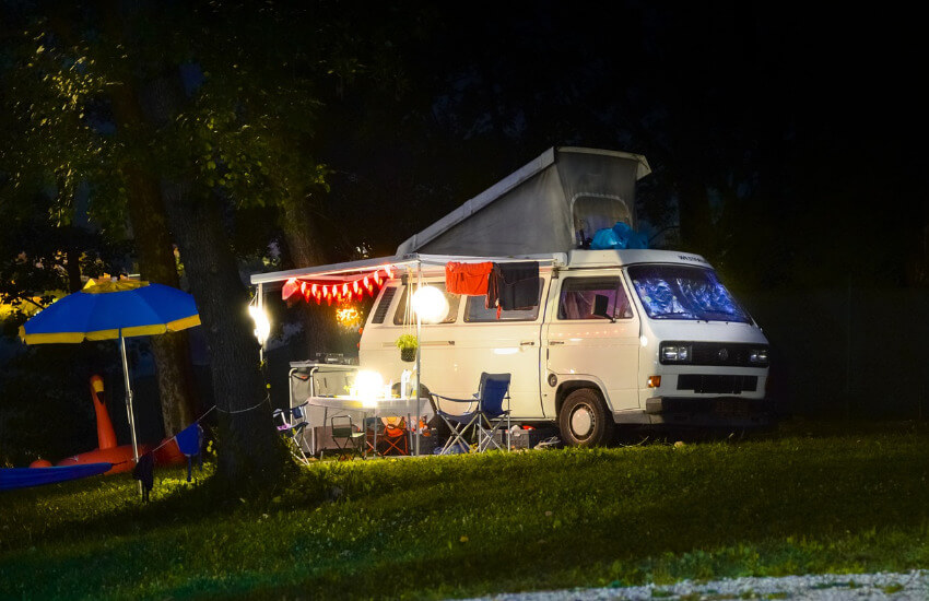 Ein Camper mit einem beleuchteten Sonnenvordach in der Nacht.