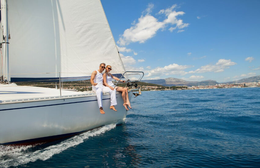 Eine Frau und ein Mann sitzen weiß gekleidet auf der Kante einer Segelyacht.