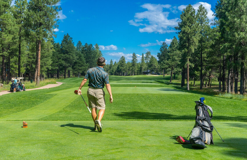 Ein schmaler Grünstreifen zwischen Bäumen, wo ein Golfspieler gerade einen Abschlag macht.
