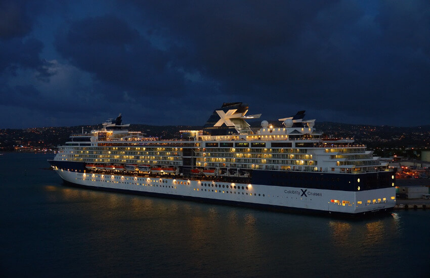 Ein beleuchtetes Kreuzfahrtschiff ankert bei nach am Hafen.