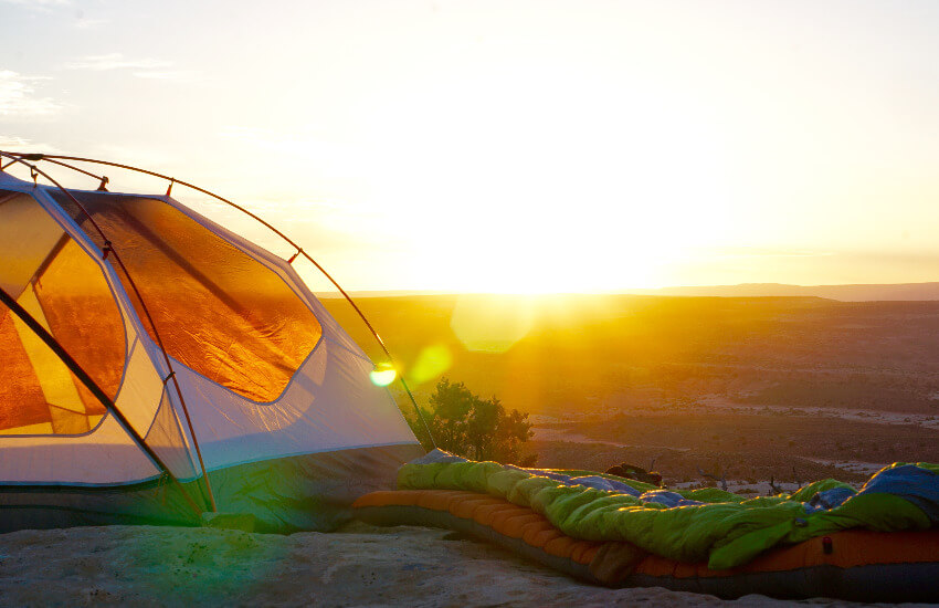 Ein Zelt, daneben eine Luftmatratze mit einem Schlafsack oben drauf während des Sonnenaufgangs.
