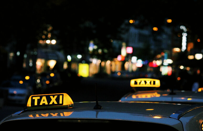 Zwei parkende Autos in der Nacht mit einem gelb leuchtenden Taxischild.