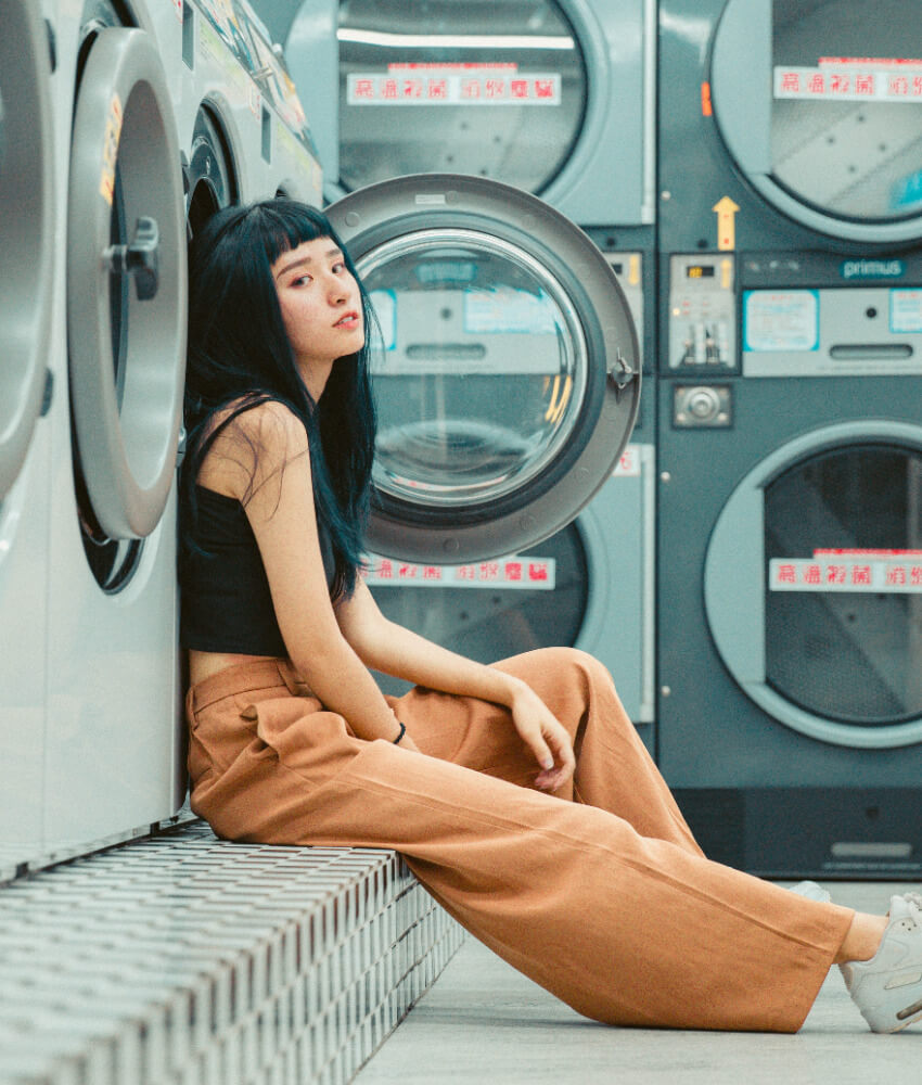 Eine Frau sitzt vor einer Waschmaschine im Waschsalon und wartet, bis die Wäsche fertig ist.
