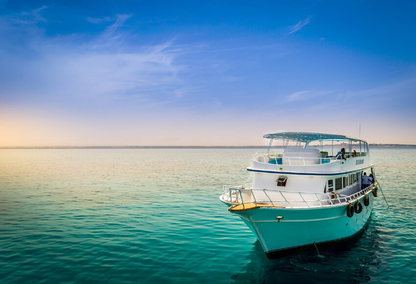 Ein weißes Boot ankert am Roten Meer unter blauem Himmel.