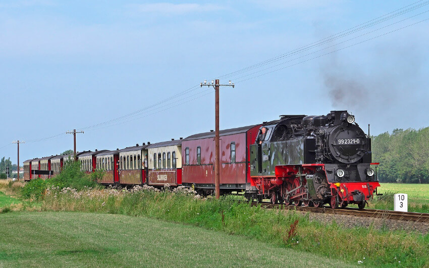 Ein alter Dampfzug unterwegs durch grüne Landschaft.