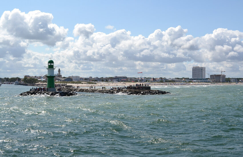 Meer mit leichtem Wellengang dahinter ist ein Leuchtturm und ein Sandstrand zu sehen.