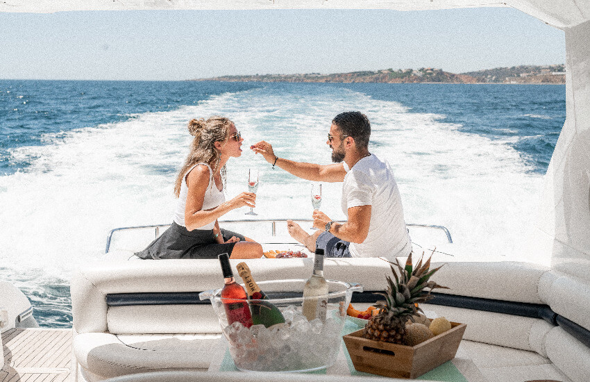 Eine Frau und ein Mann genießen Sekt und Früchte auf dem Heck einer Yacht.