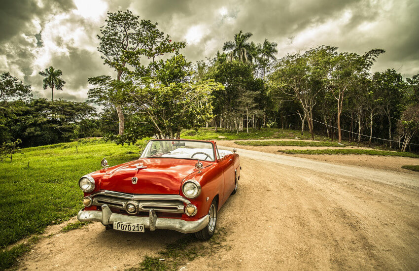 Rotes Oldtimer-Cabrio parkt auf einem Feldweg in Kuba vor grüner, tropischer Vegetation.