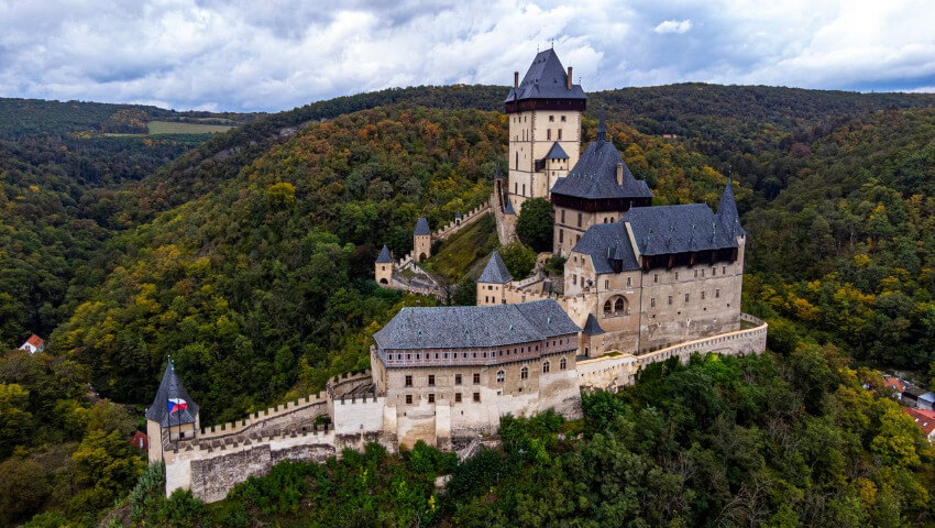 Drohnenaufnahme der Burg Karlstein in Tschechien, umgeben von dichten Wäldern.